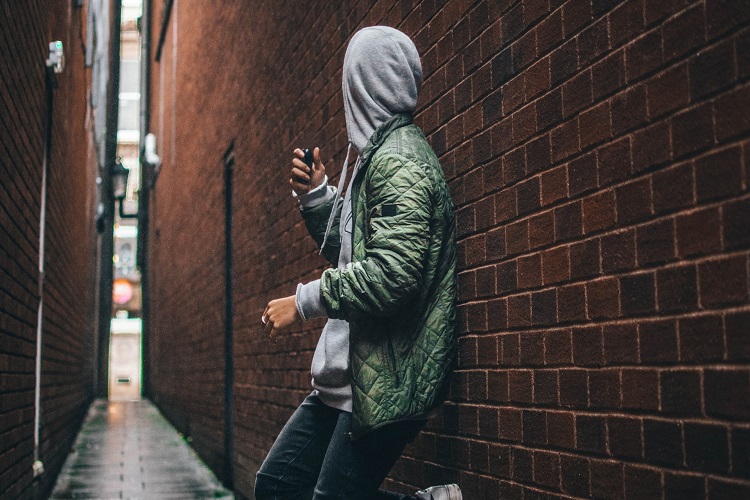 Man wearing green hooded jacket standing beside the wall